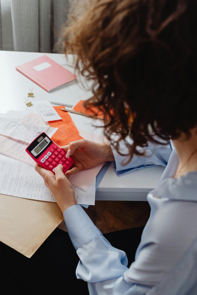 pexels-photo-7680683-7680683 Adult woman working with receipts and a bright pink calculator at a desk, focusing on finances.